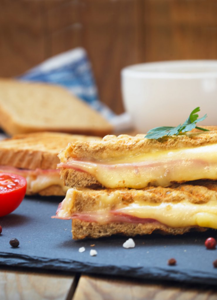 Club sandwiches for quick breakfast. Grilled or toasted sandwiches with ham salami, tomato and melted cheese. Cup of coffee in the background.